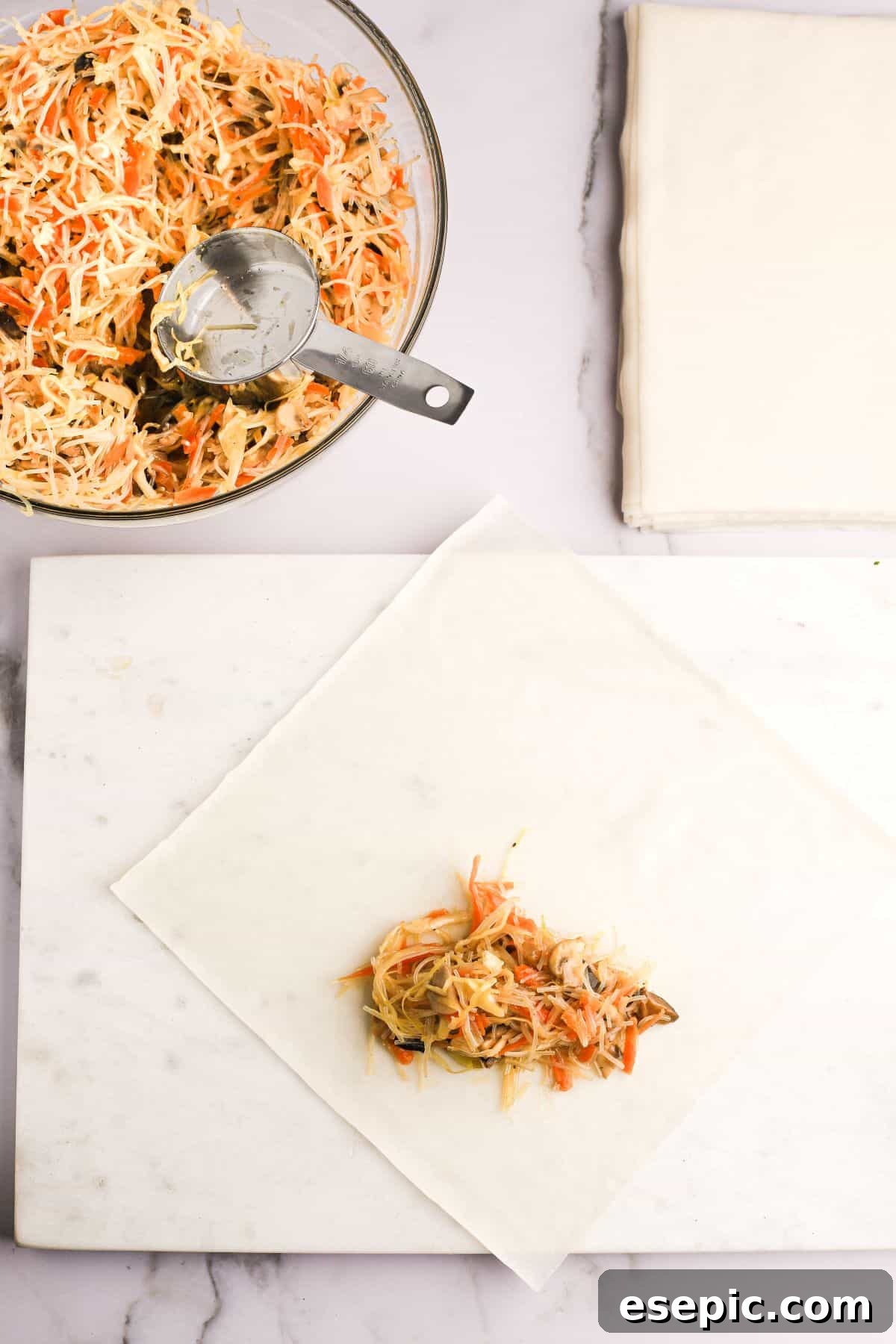 A spring roll wrapper carefully laid out on a clean work surface, with a small, neatly placed mound of savory vegetable filling positioned in the bottom corner, ready for the folding process.