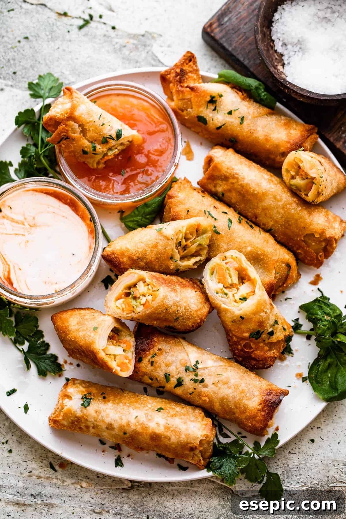 A beautifully presented plate of golden veggie spring rolls, served alongside a small bowl of sweet chili dipping sauce, inviting a delicious culinary experience.