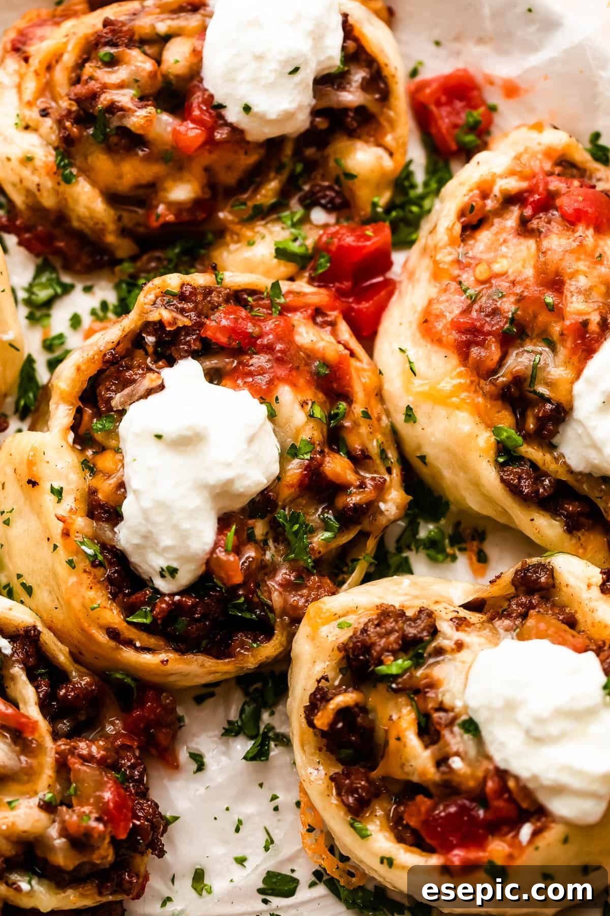 Cheesy Baked Taco Swirls 3 Overhead shot of freshly baked taco pinwheels topped with diced tomatoes and a dollop of sour cream, garnished with cilantro.