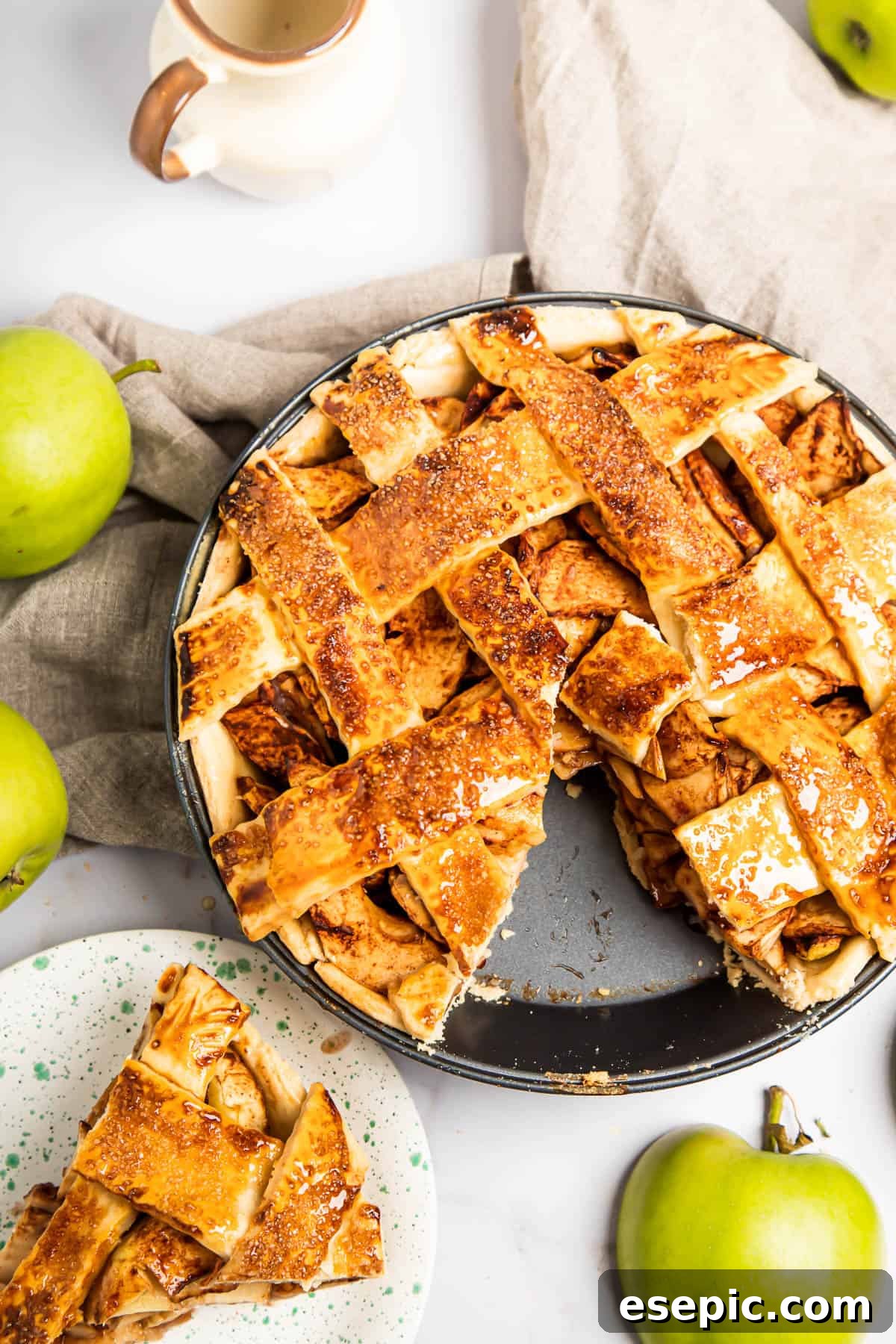 This classic yet easy and delicious Apple Pie recipe is made from scratch, with a buttery, flaky pie crust, fresh apple slices, pie spices, and brown sugar. A beautiful homemade apple pie with a slice carefully removed, showcasing the golden filling and flaky crust. The slice sits on a nearby saucer.