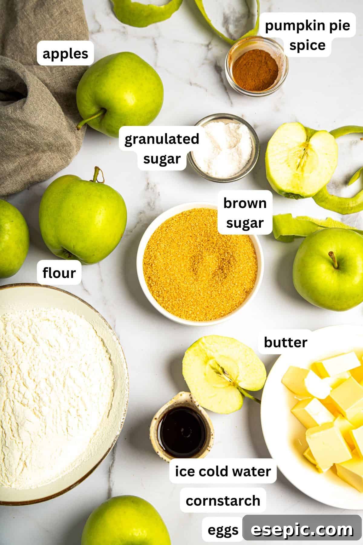 This classic yet easy and delicious Apple Pie recipe is made from scratch, with a buttery, flaky pie crust, fresh apple slices, pie spices, and brown sugar. An overhead view of various fresh ingredients laid out on a kitchen counter, ready for making homemade apple pie, including apples, flour, butter, and spices.