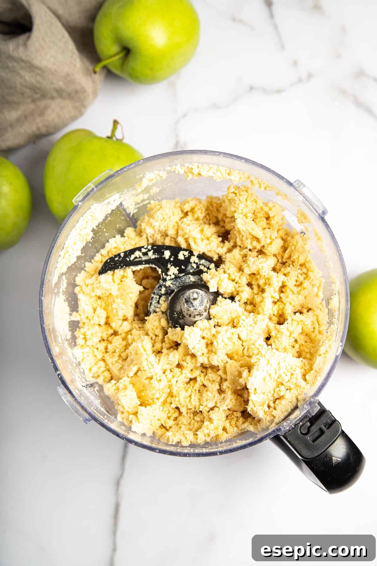 This classic yet easy and delicious Apple Pie recipe is made from scratch, with a buttery, flaky pie crust, fresh apple slices, pie spices, and brown sugar. Pie crust dough being combined in a food processor, resembling coarse breadcrumbs.