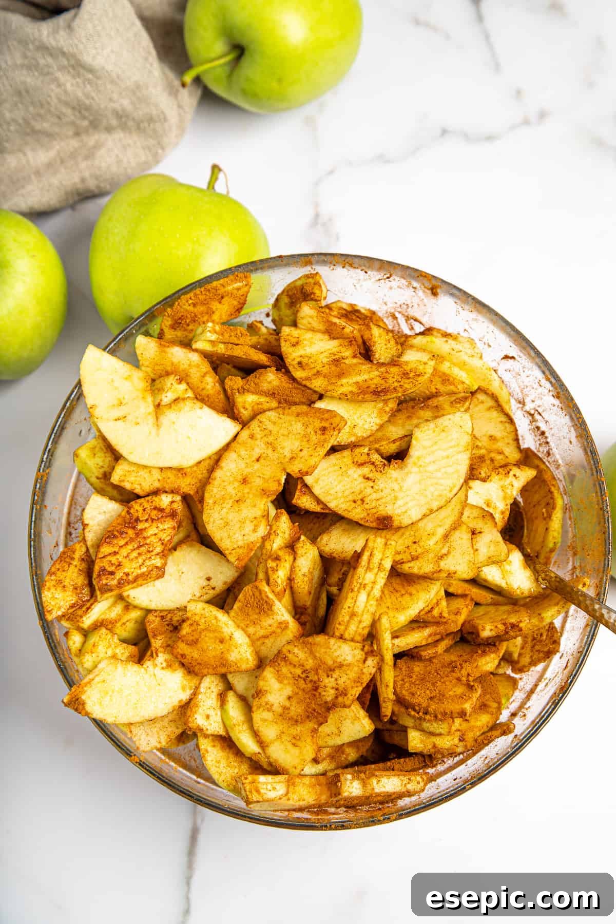 This classic yet easy and delicious Apple Pie recipe is made from scratch, with a buttery, flaky pie crust, fresh apple slices, pie spices, and brown sugar. Thinly sliced apples coated with a mixture of cornstarch, sugar, and warm spices in a mixing bowl.