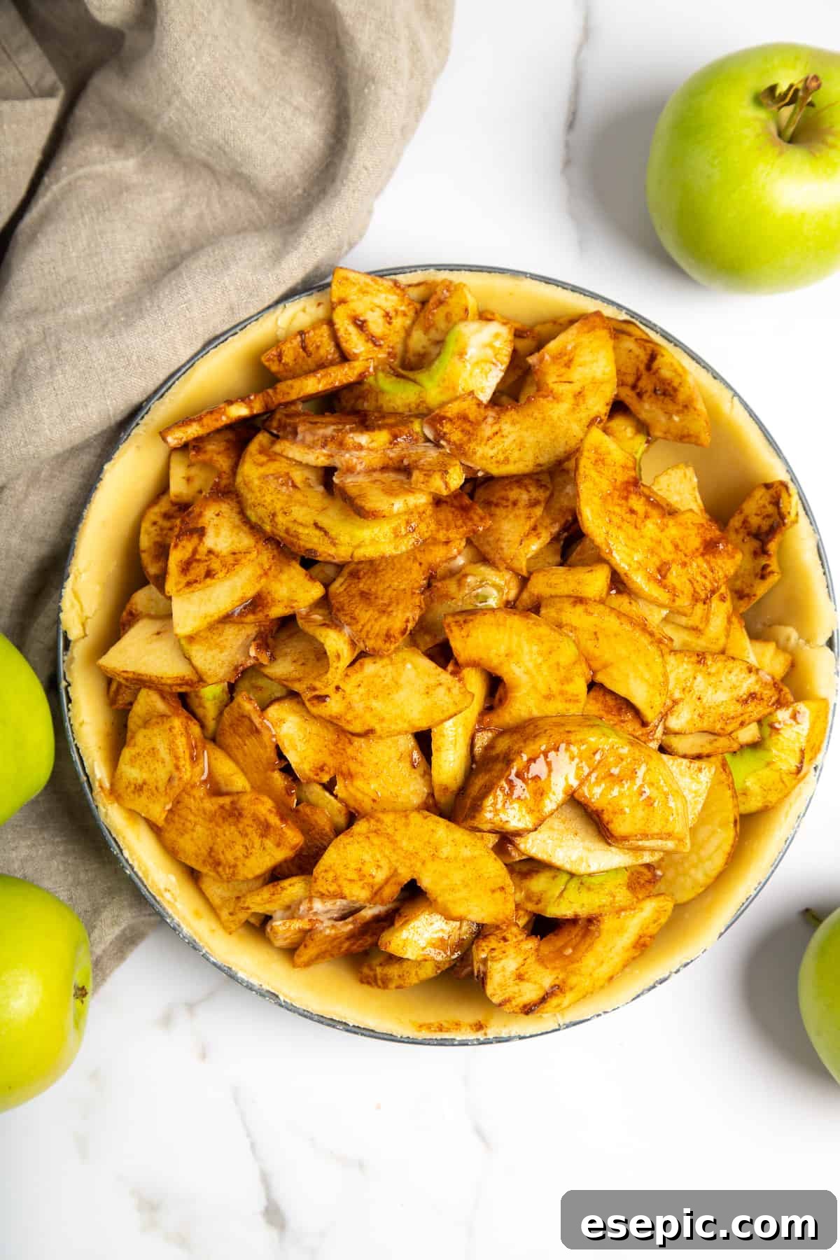 This classic yet easy and delicious Apple Pie recipe is made from scratch, with a buttery, flaky pie crust, fresh apple slices, pie spices, and brown sugar. A generous mound of apple pie filling nestled within an unbaked pie crust in a pie plate.