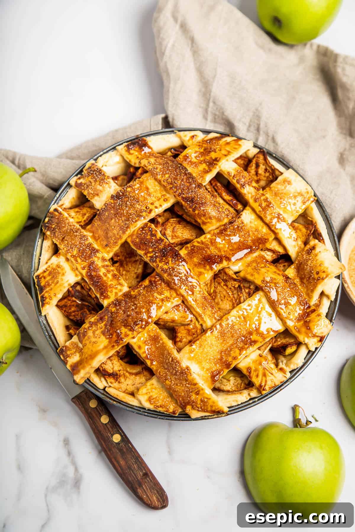 This classic yet easy and delicious Apple Pie recipe is made from scratch, with a buttery, flaky pie crust, fresh apple slices, pie spices, and brown sugar. A freshly baked homemade apple pie with a golden-brown lattice top, sitting on a wooden surface.