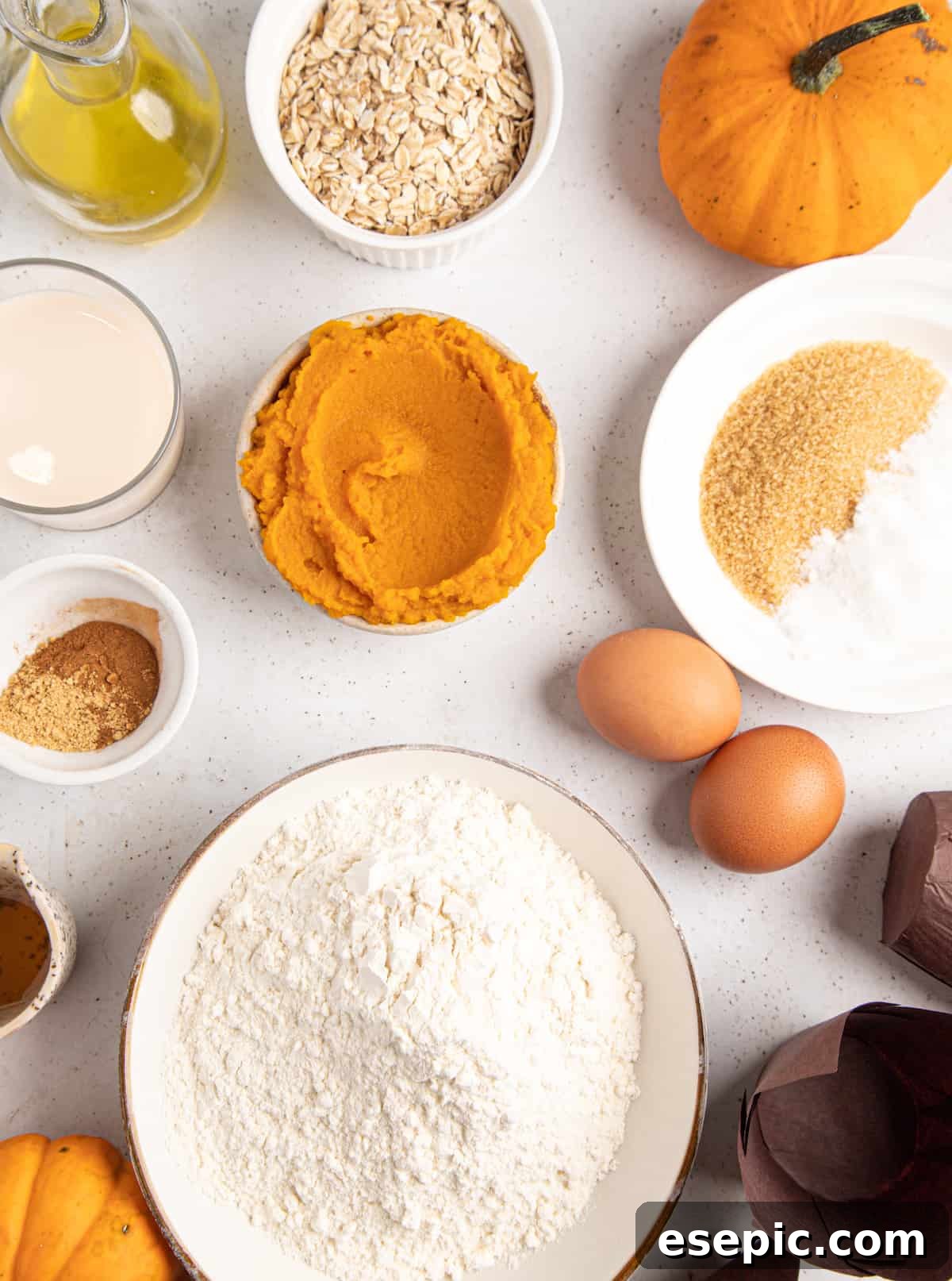 An array of fresh baking ingredients neatly arranged on a counter, including flour, sugar, eggs, sour cream, honey, melted butter, oats, and various spices, all ready for making pumpkin muffins.