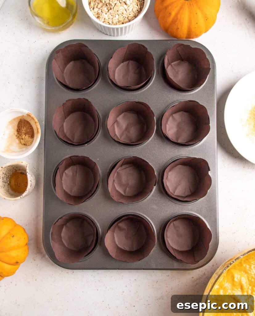 A prepared muffin pan with twelve rustic dark brown paper liners, ready to be filled with pumpkin muffin batter.