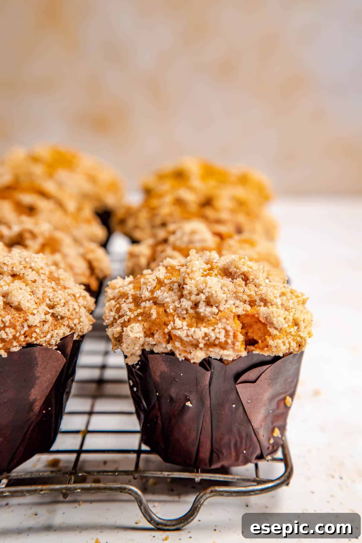 Freshly baked pumpkin muffins cooling on a wire rack, still steaming slightly, with their golden crumble tops in clear view.