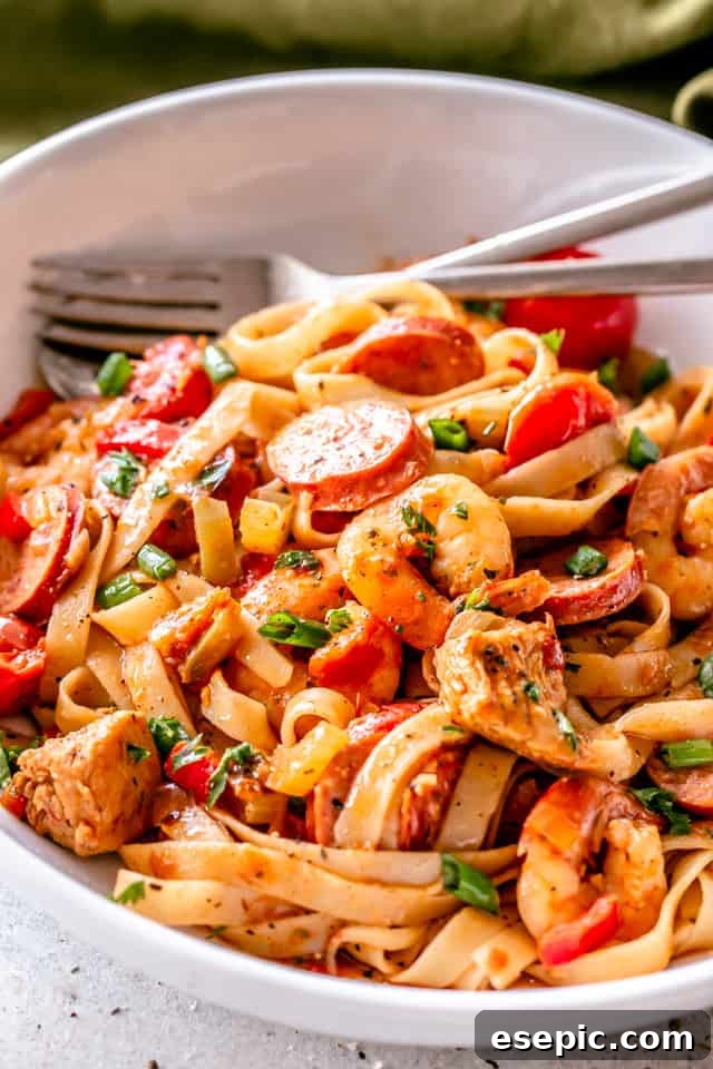 A serving of One Pot Jambalaya Pasta in a white bowl, showing the rich sauce, pasta, chicken, sausage, and shrimp.