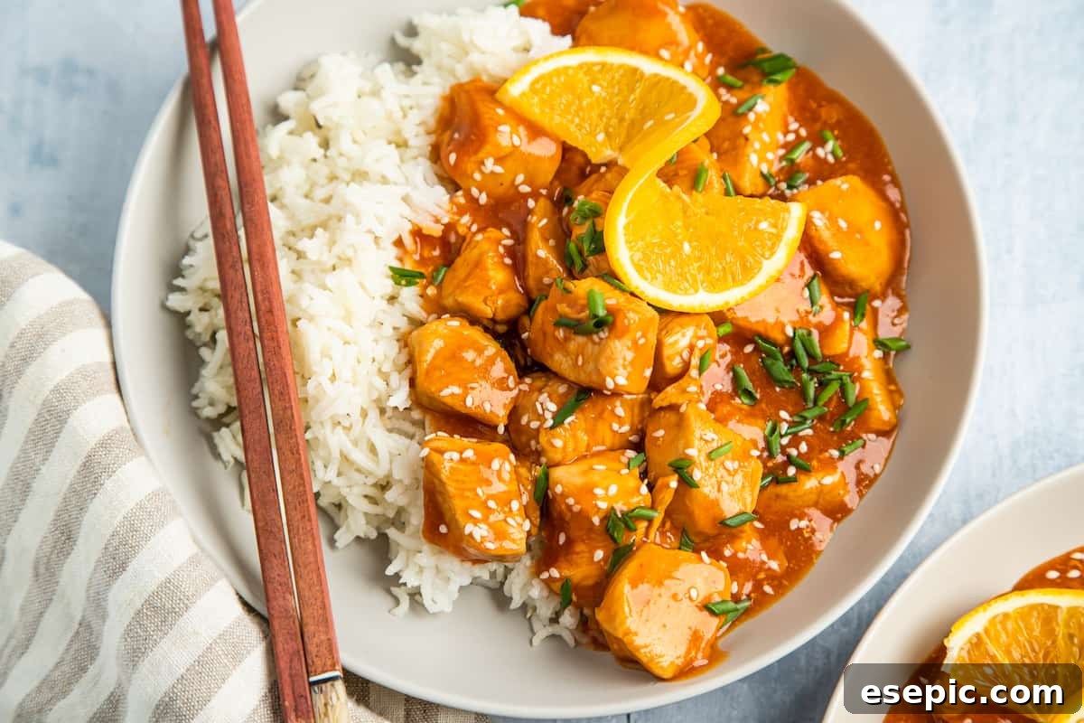 Effortless Instant Pot Orange Chicken 8 a serving of orange chicken, garnished with orange wedges, on a plate with white rice and chopsticks.