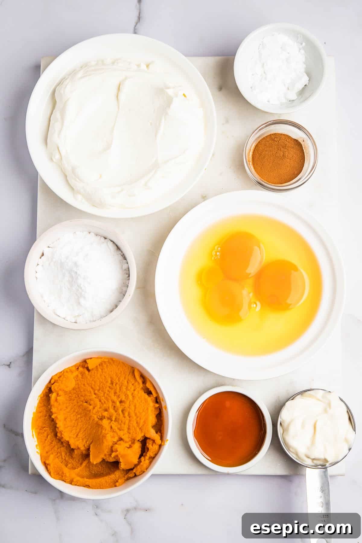 Spiced Instant Pot Pumpkin Cheesecake 3 Overhead shot of various bowls containing fresh ingredients for Instant Pot Pumpkin Cheesecake, including cream cheese, pumpkin puree, eggs, and spices, ready for mixing.
