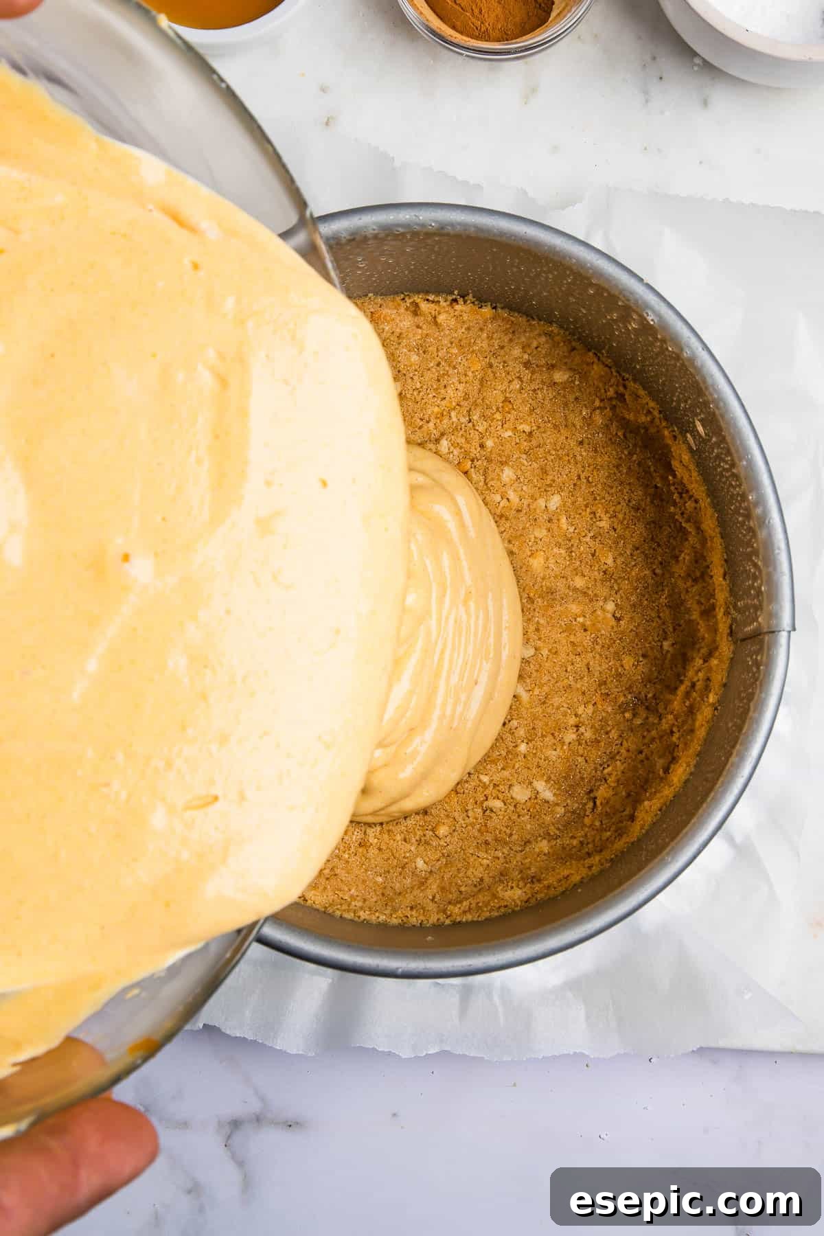Irresistible Instant Pot Pumpkin Cheesecake 4 Pouring the creamy pumpkin cheesecake batter over the prepared graham cracker crust inside a springform pan.