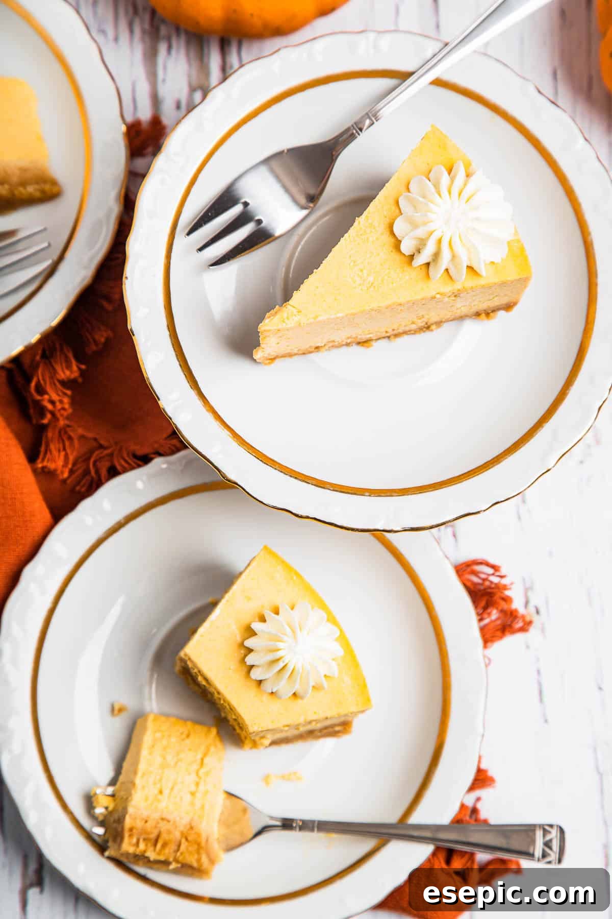 Irresistible Instant Pot Pumpkin Cheesecake 7 An overhead shot featuring two plates, each holding a delectable slice of pumpkin cheesecake garnished with a swirl of whipped cream.