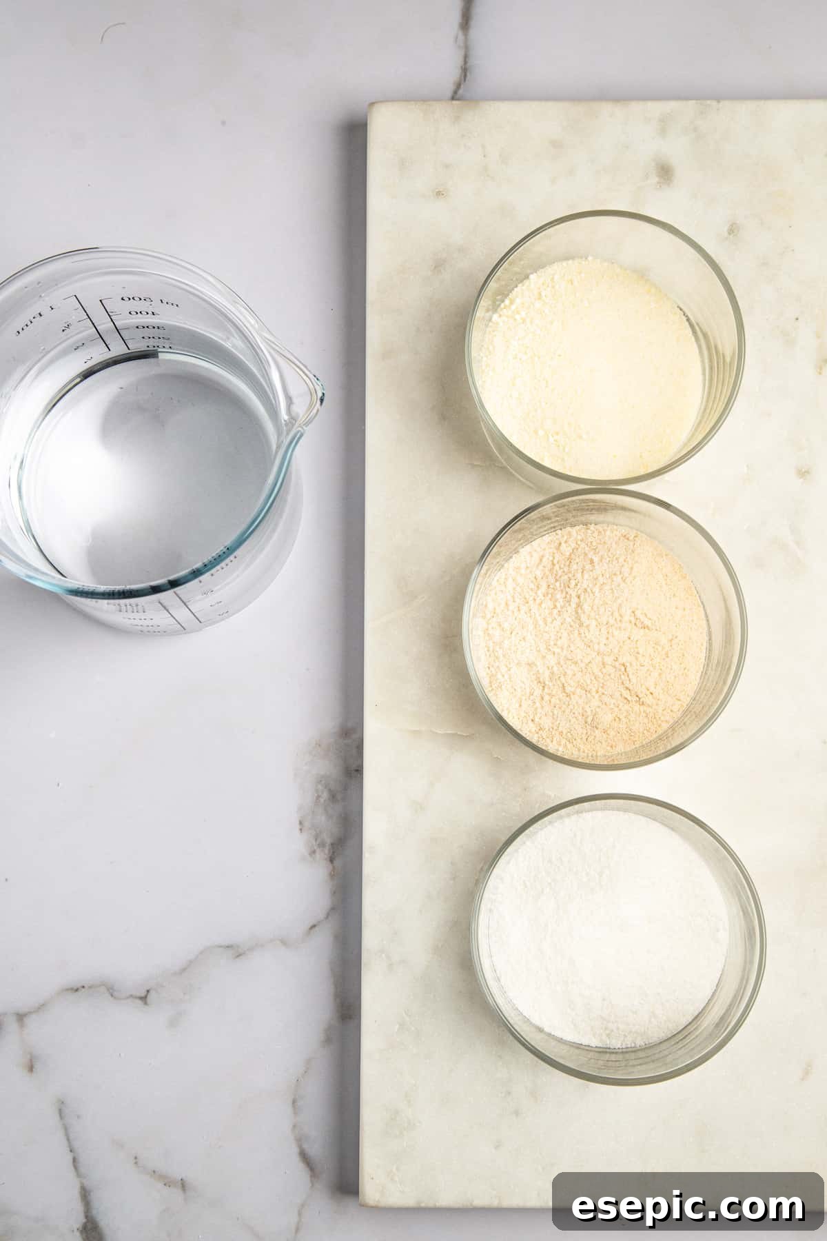 Three small containers of flavored gelatin mixes and a clear measuring cup filled with vodka, arranged on a surface.