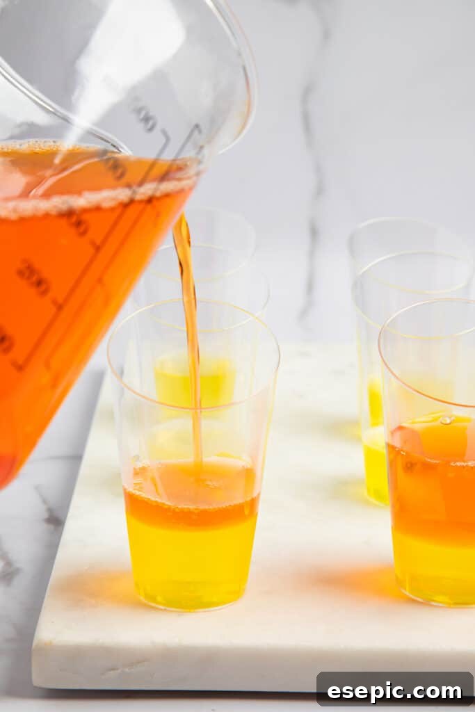 Vibrant orange jello being added to shot glasses, carefully layered over the already set lemon jello.