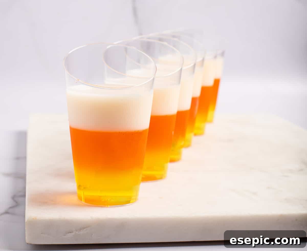 A perfectly aligned row of candy corn jello shots, showcasing their distinct yellow, orange, and white layers.