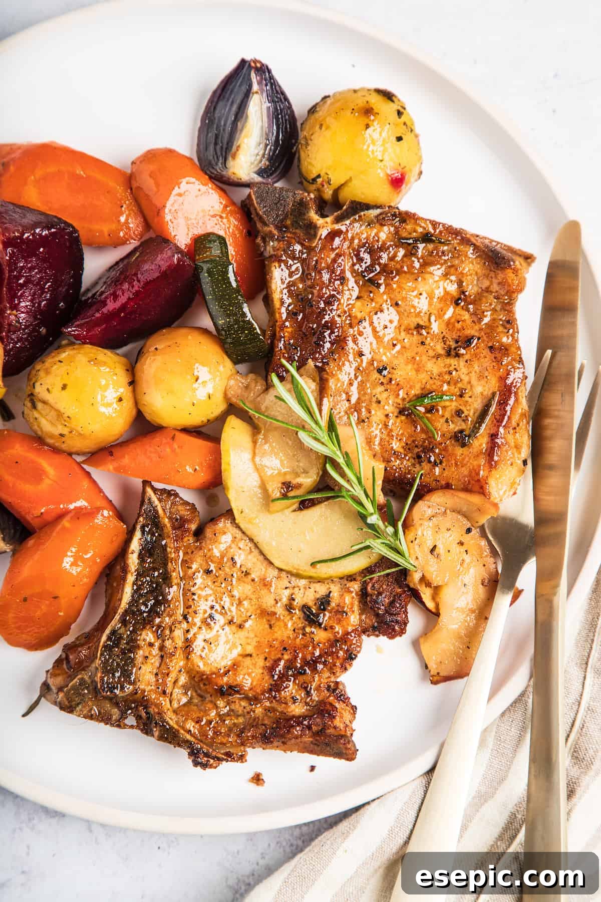 Roasted Pork Chops with Apples and Root Vegetables 2 A plate of baked pork chops with apples and winter vegetables, garnished with a sprig of rosemary, ready to be served.