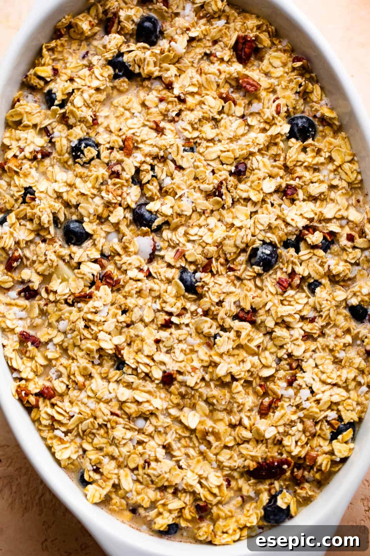 oval baking dish with uncooked oatmeal with berries and apples