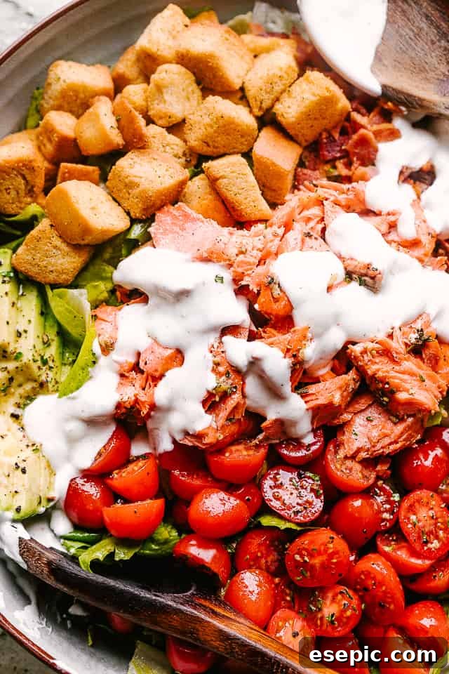 Close-up of a Salmon BLT salad, showcasing the golden salmon flakes, crispy bacon bits, and vibrant cherry tomatoes, all coated in a rich dressing.