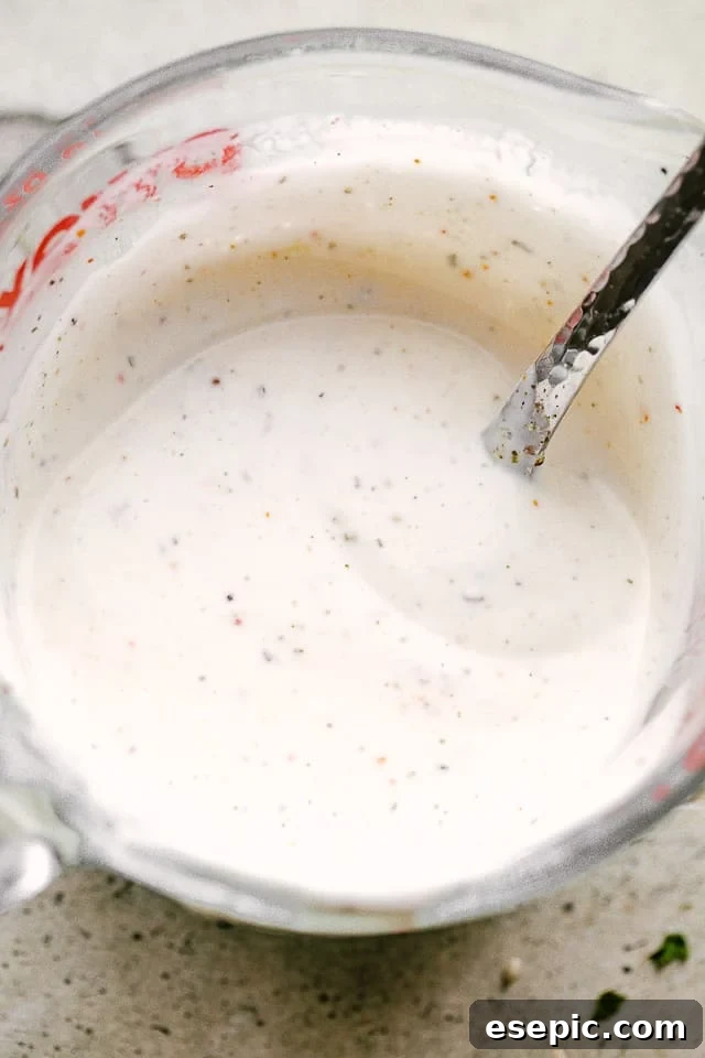 Creamy mayonnaise-based homemade ranch dressing in a clear mixing cup with a spoon, ready for the Salmon BLT Salad.