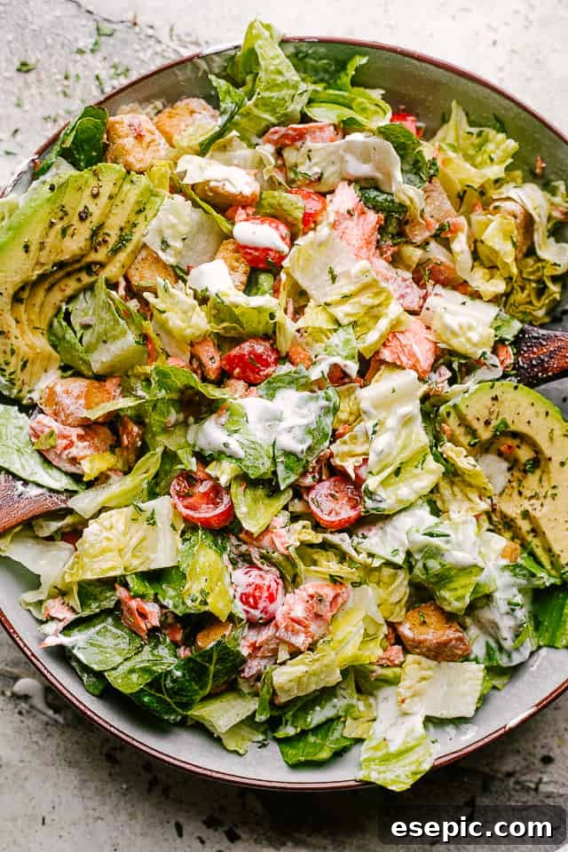 Full view of a Salmon BLT salad in a white bowl, with dressing drizzled, showcasing its vibrant ingredients and inviting presentation.