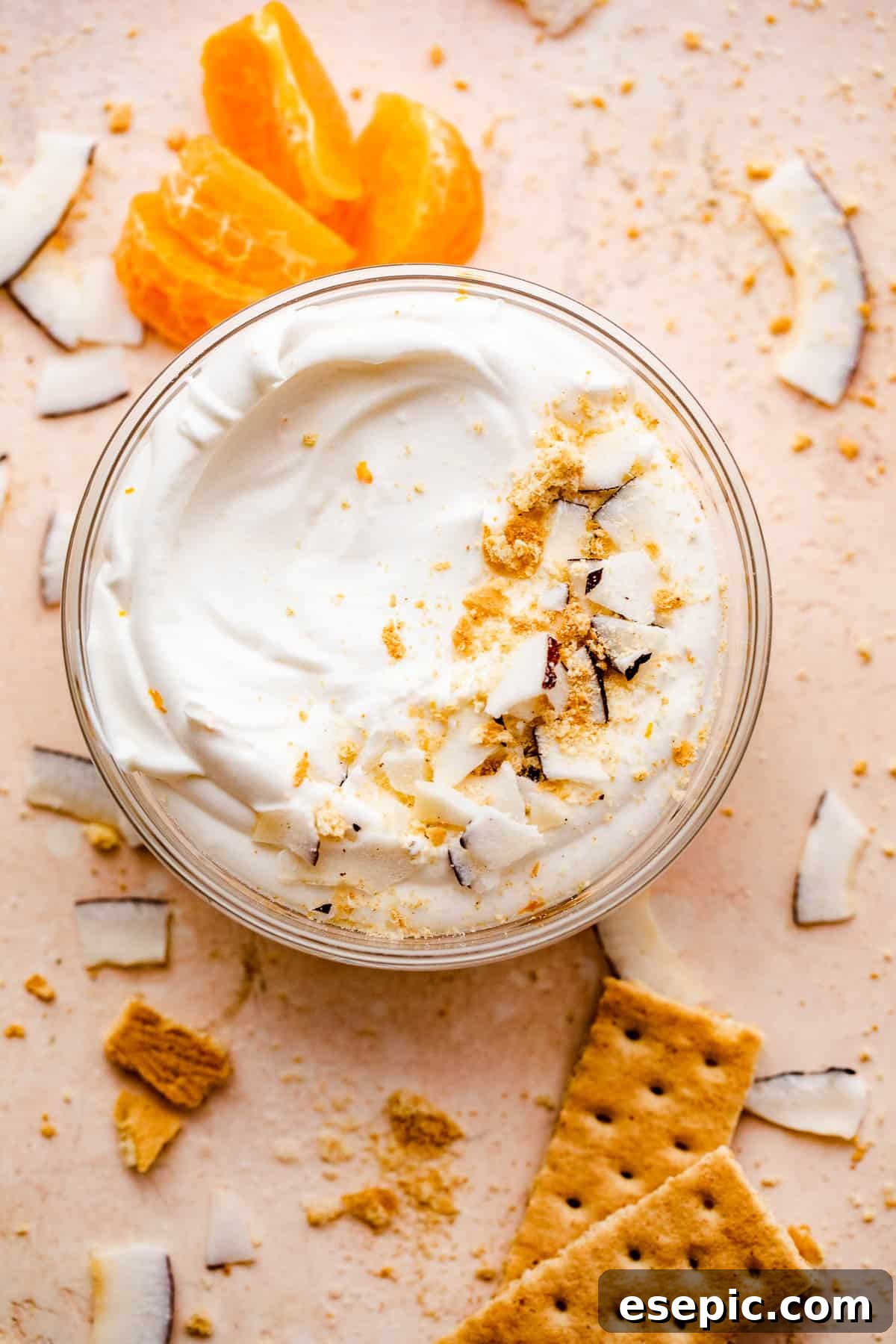 An overhead shot showcasing a glass bowl filled with creamy coconut dip, beautifully garnished with fresh tangerine slices and delicate coconut shavings around and on the edges of the bowl.