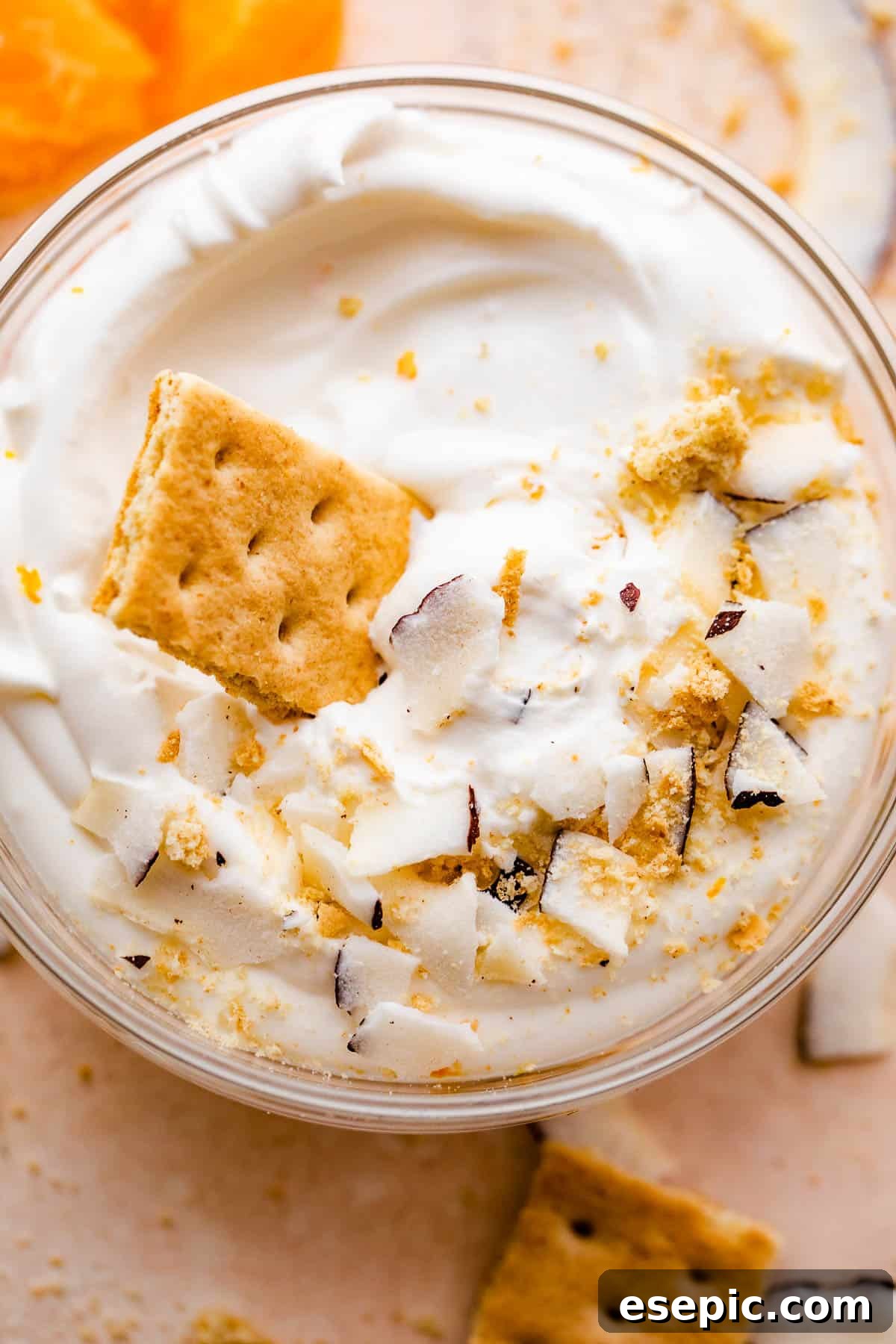 An overhead view of a glass bowl filled with creamy coconut dip, artfully arranged with tangerine slices and delicate coconut shavings around its perimeter and on top.