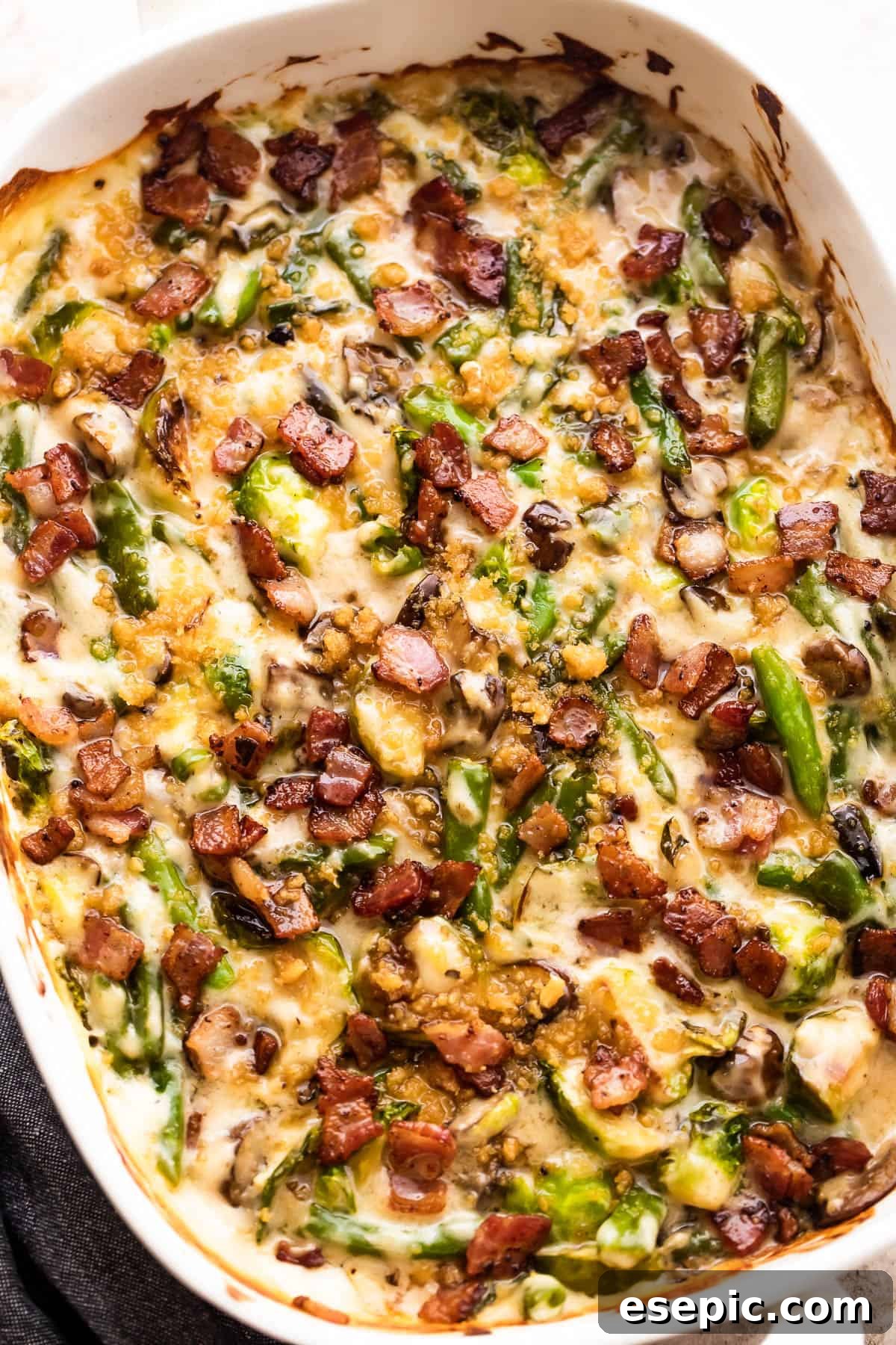 Overhead view of a baked green bean and Brussels sprouts casserole, generously topped with diced bacon and golden breadcrumbs.