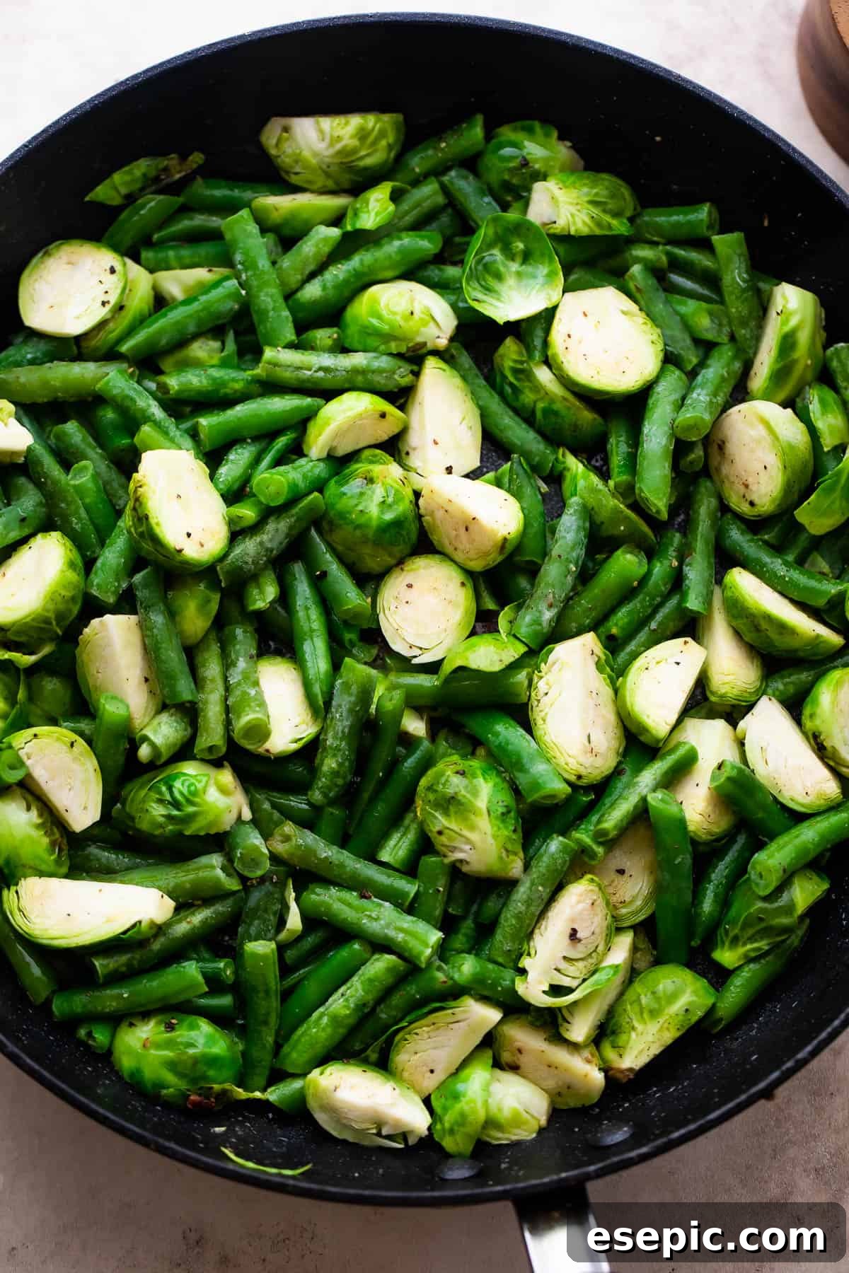 Sautéing fresh Brussels sprouts and green beans in a large black skillet with bacon grease.