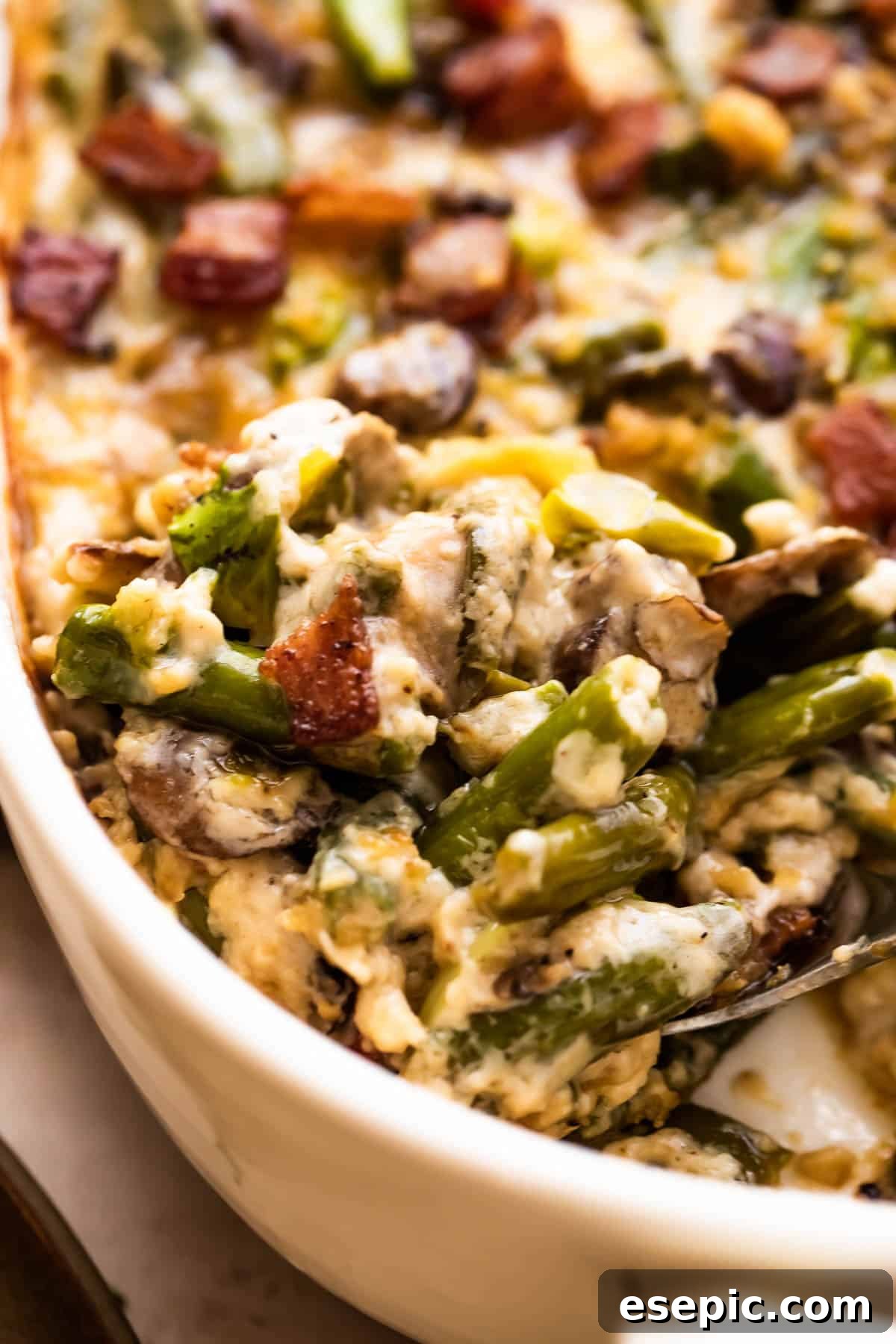 Close-up of a large serving spoon scooping out a generous portion of warm, creamy green bean casserole from a white dish.