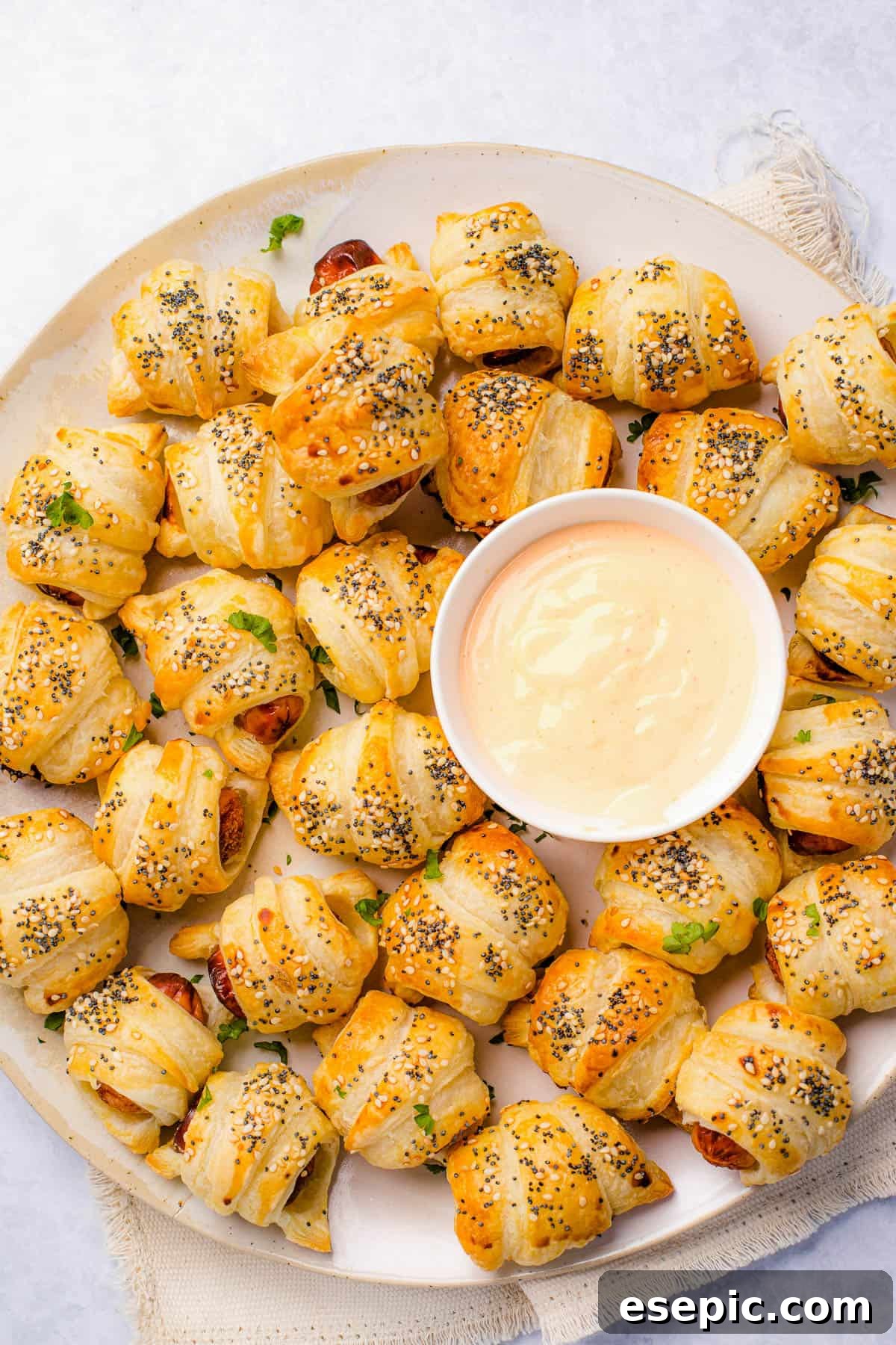 Super easy to make homemade Pigs in a Blanket are a delicious snack prepared with savory mini-sausages wrapped in golden, flaky puff pastry. A platter of pigs in a blanket with a bowl of dipping sauce in the center.