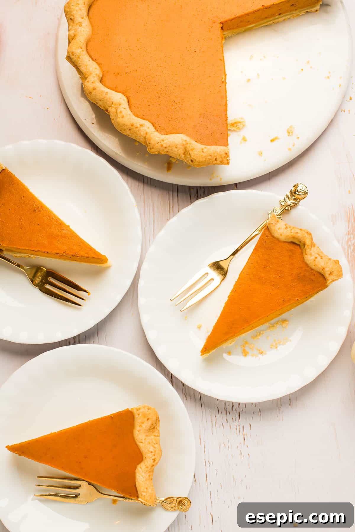 This homemade Pumpkin Pie recipe, featuring a tender crust, warm spices, and dulce de leche pumpkin filling, is an effortless holiday favorite everyone will adore. A perfectly baked pumpkin pie in a white serving platter with one slice carefully removed and placed on a smaller dessert plate, accompanied by a golden fork. The crust is golden brown and crimped beautifully.