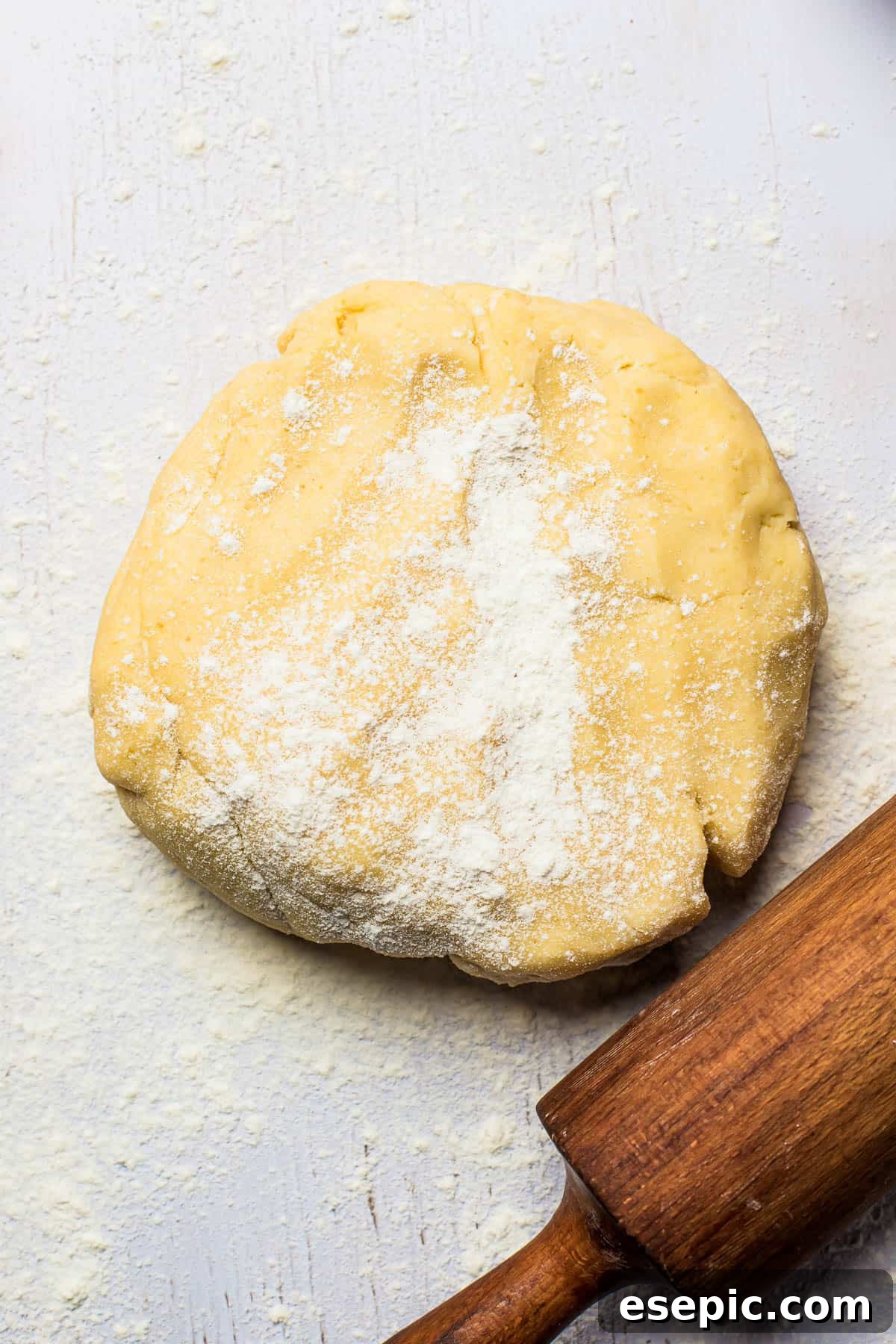 Learn how to make the perfect homemade pie crust for your pumpkin pie, ensuring a tender, flaky base for your festive dessert. Freshly prepared pie dough resting on a floured surface next to a wooden rolling pin, ready to be shaped.