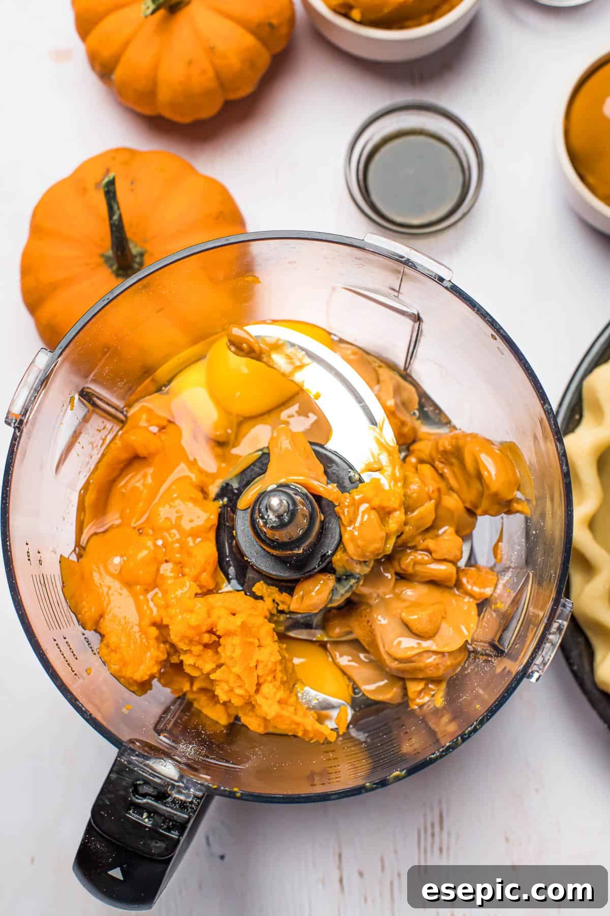 Combining all the delicious ingredients for a smooth and creamy pumpkin pie filling, ready to be poured into the crust. All the pumpkin pie filling ingredients, including canned pumpkin puree, dulce de leche, eggs, and spices, are combined in a blender on a pristine white work surface, surrounded by decorative mini pumpkins.