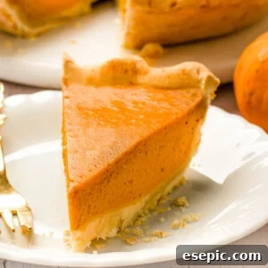 A delicious slice of homemade pumpkin pie with a golden crust on a white plate, ready to be served.