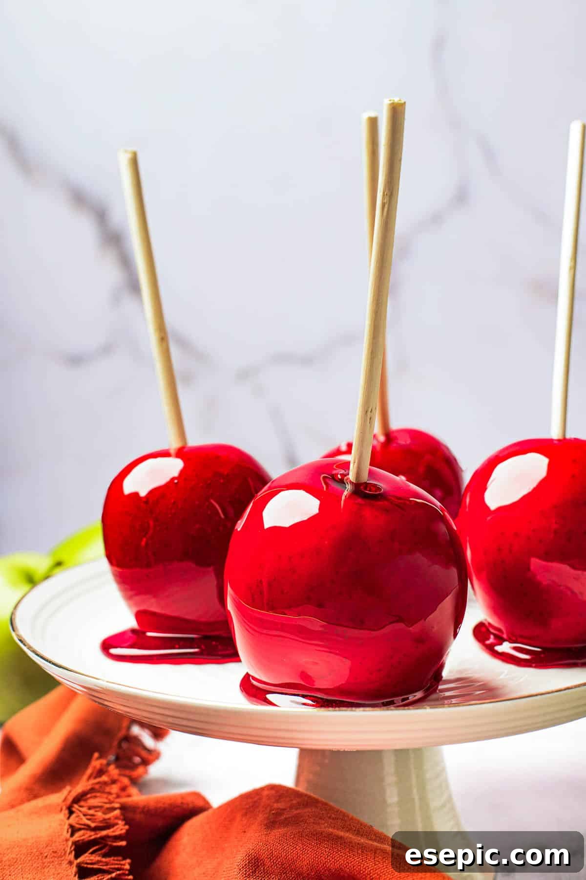 Sweet And Crunchy Candy Apples From Scratch 3 A white cake stand with four candied apples displayed on it.