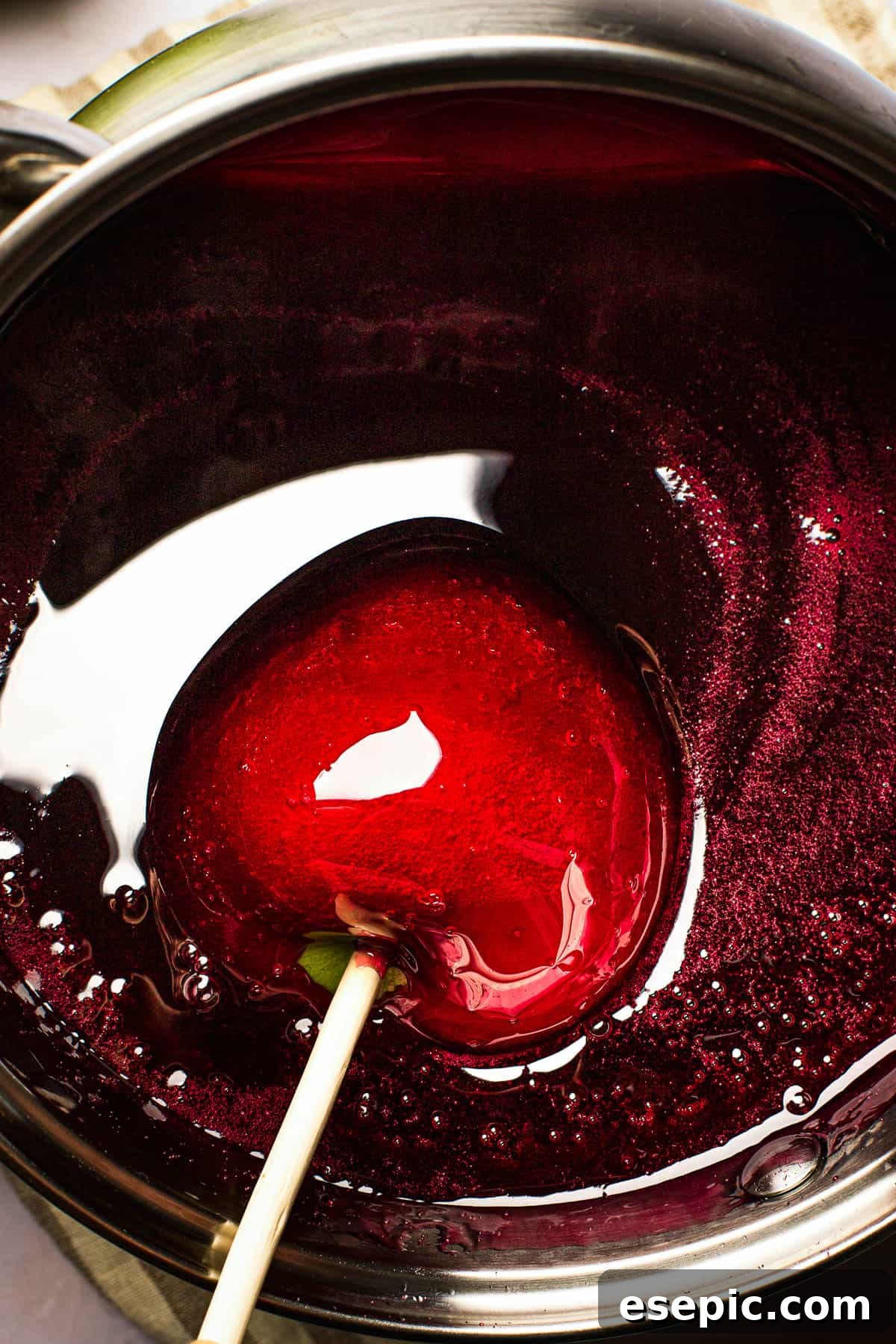 Sweet And Crunchy Candy Apples From Scratch 7 An apple coated in red candy is being lifted from a saucepan of the candy mixture.