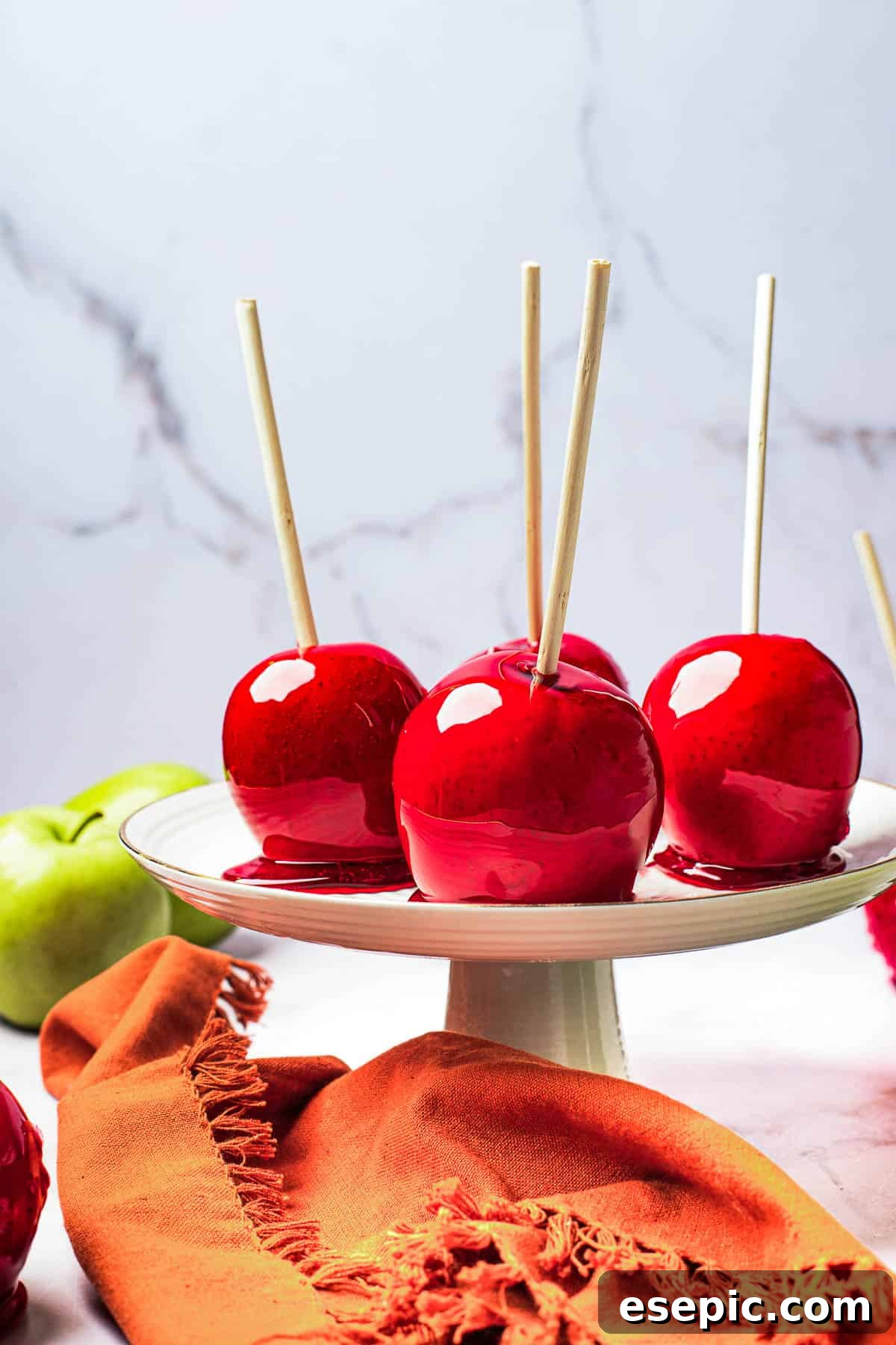 Sweet And Crunchy Candy Apples From Scratch 9 A white cake stand with four candied apples displayed on it.