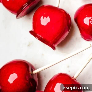 Several candy apples on a white cutting board. Plain Granny Smith apples and an orange fringed placemat in the background.