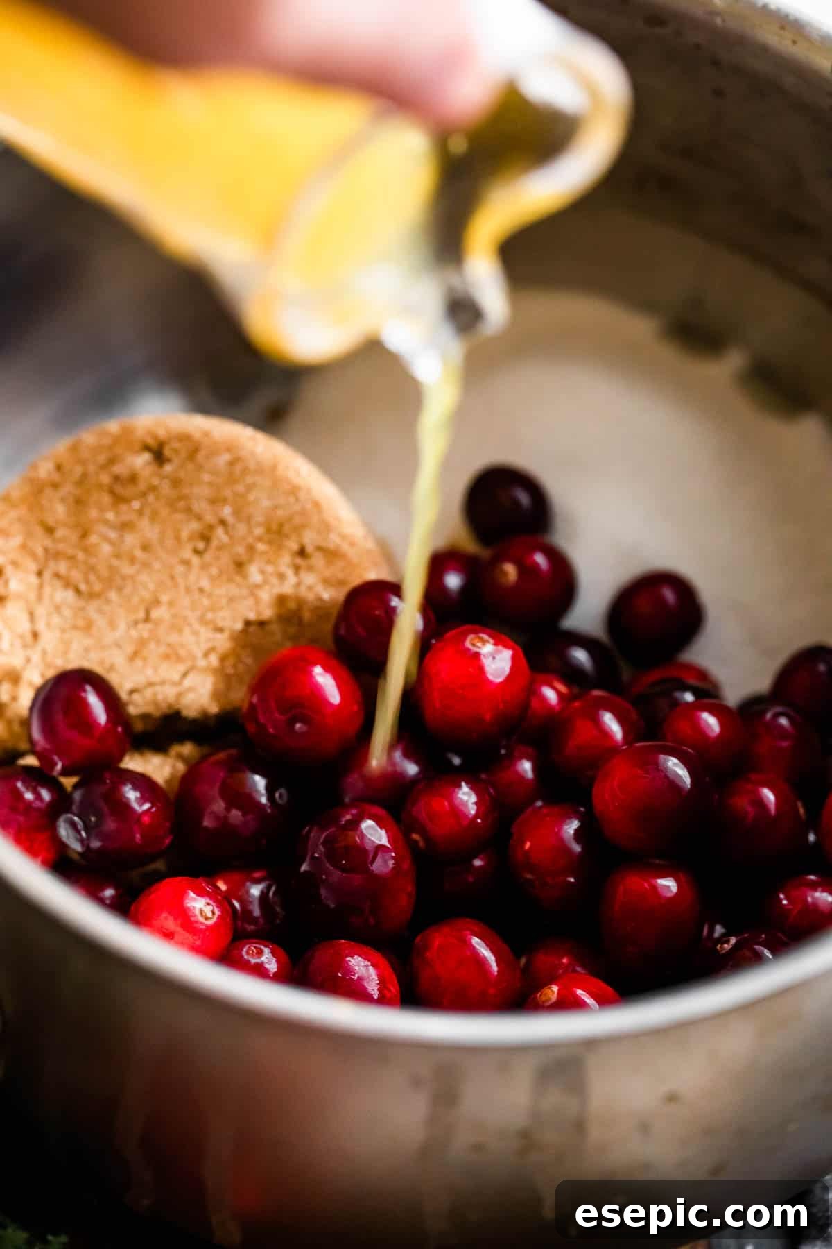 pouring orange juice over fresh cranberries and sugars inside of a saucepan.