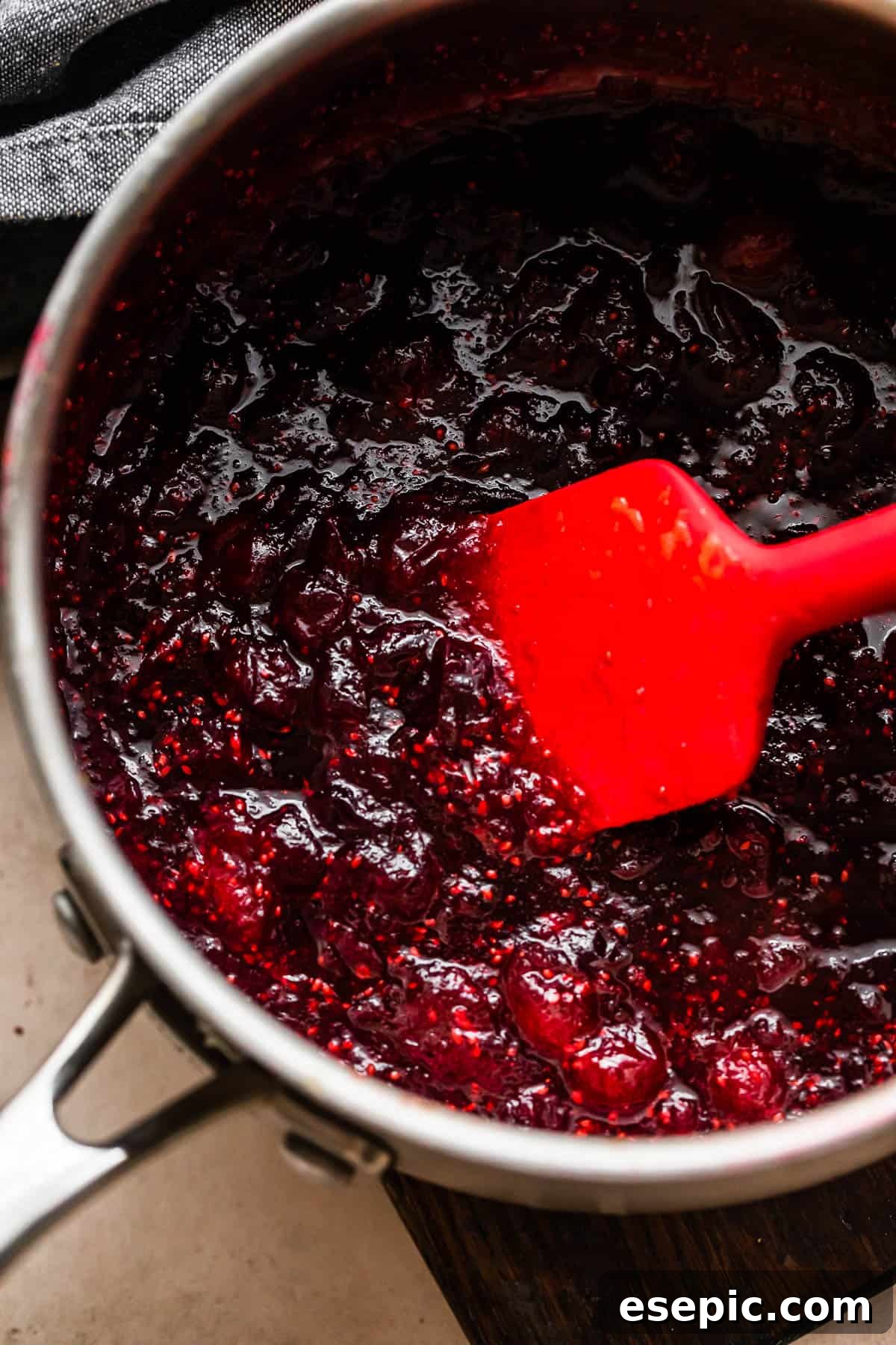 cooking cranberry sauce in a saucepan and stirring through with a red rubber spatula.