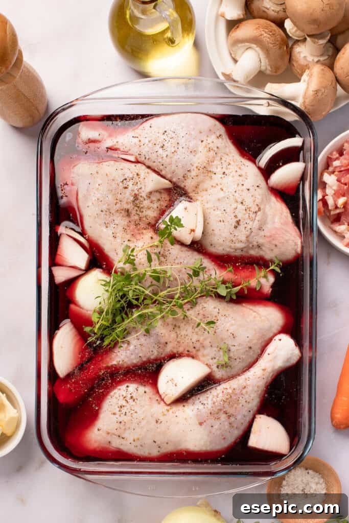 Quick and Classic Instant Pot Coq au Vin 4 A glass baking dish with chicken leg quarters, quartered onions, and fresh thyme, all marinating in red wine. The other coq au vin ingredients are arranged around the work surface.